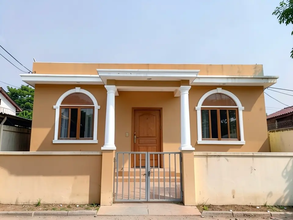 The same house with two round white columns with capitals, a heavier white molded beam over the verandah, arched white window surrounds and warm sand-orange walls; the boundary wall is also painted the wall colour