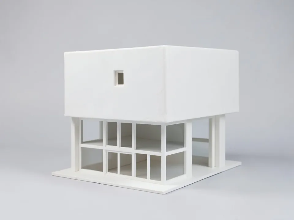 A plain white clay model of a two-storey house: a solid upper box with one small window over a ground floor of gridded glazing between posts