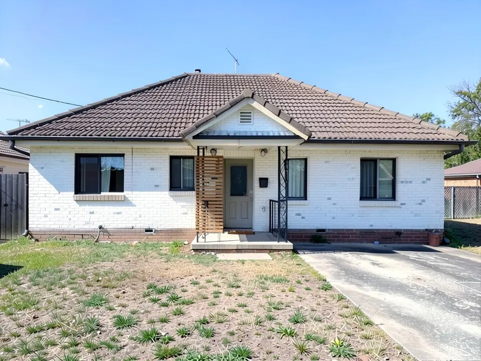 The same bungalow with the brick painted white, black window frames and a horizontal timber batten screen beside the front door; the hipped roof, the wrought-iron porch, the driveway and the patchy lawn unchanged