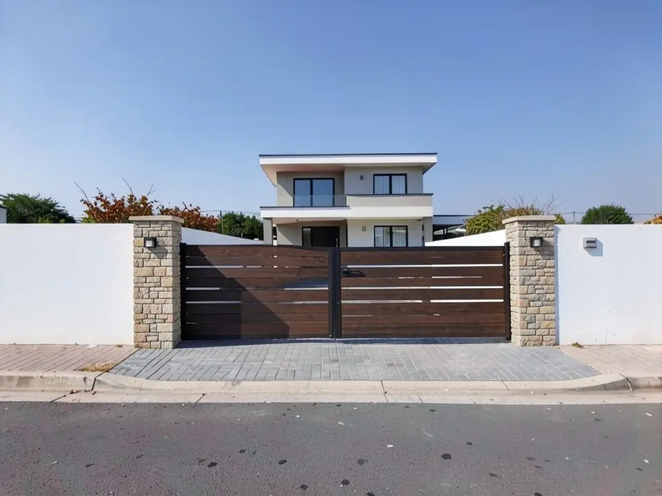 The same entrance with a closed dark timber sliding gate made of horizontal slats between two stone-clad pillars with small lights