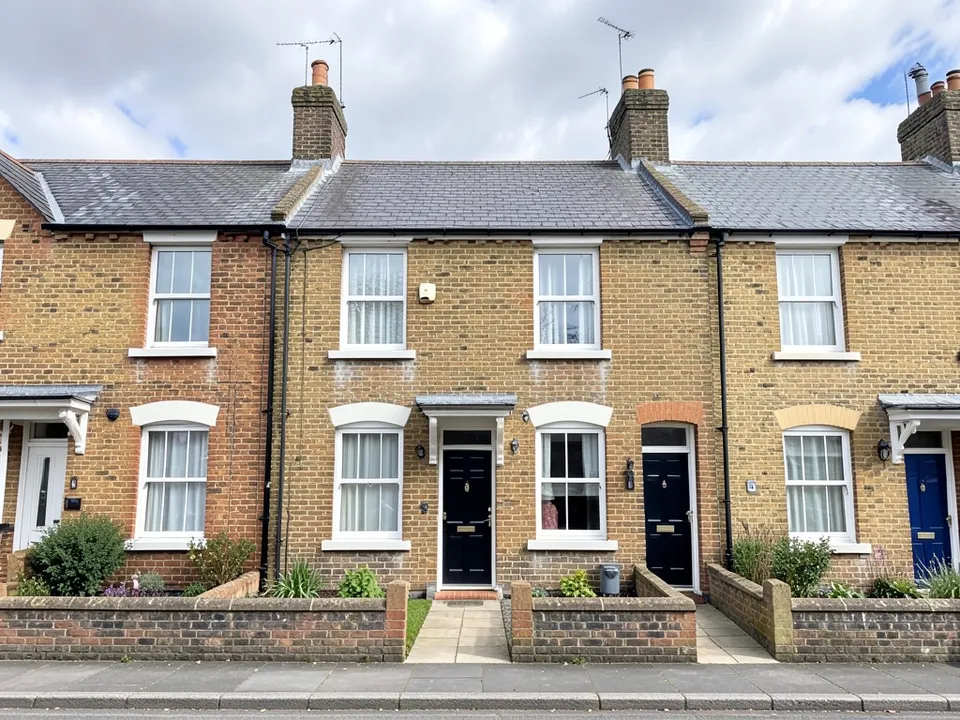 A row of plain two-storey yellow brick terraced houses with low slate roofs, white sash windows, black and blue front doors and small front gardens behind low brick walls